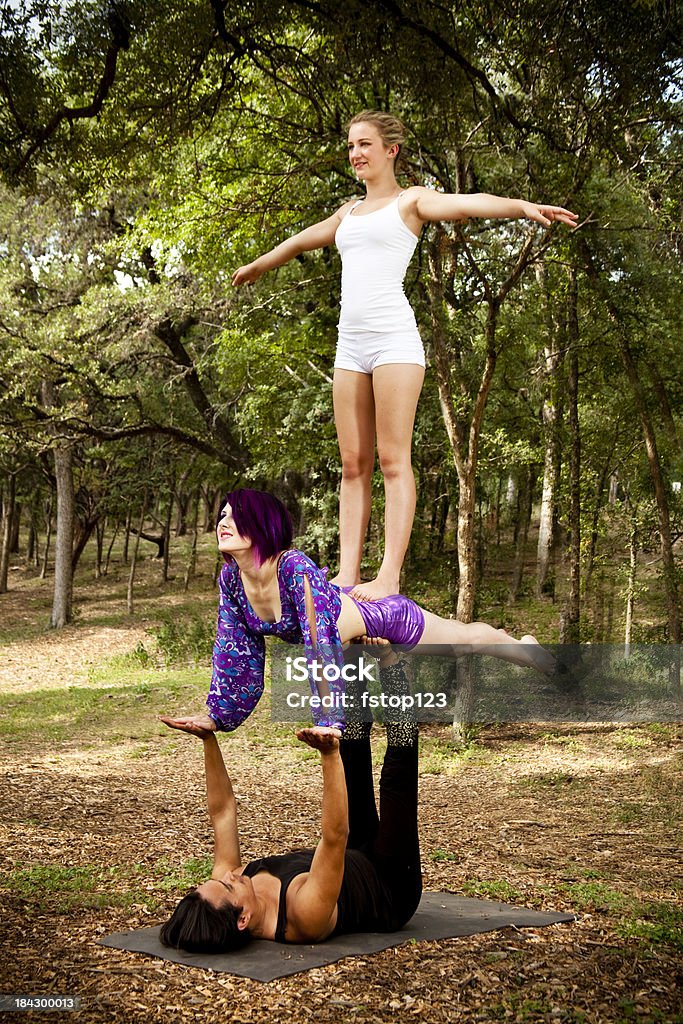 Trio di eseguire AcroYoga in un appartato legno area. - Foto stock royalty-free di A mezz'aria