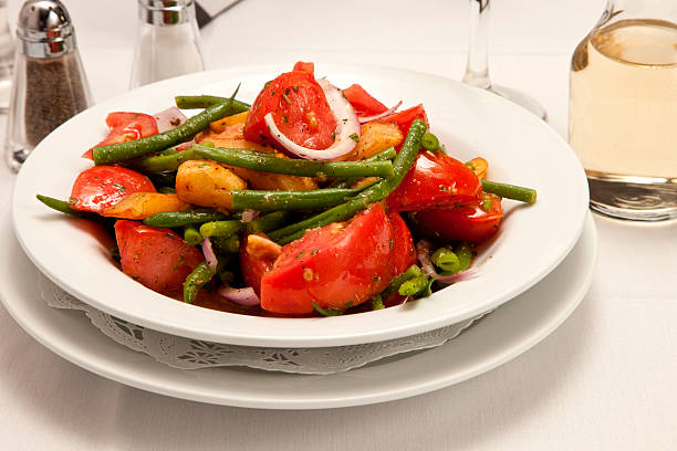 Tomato salad with string beans, onions, and potato. Delicious salad in a white dish, on a restaurant table, with a small carafe of white wine, salt and pepper.  Image shot with Canon 5D Mark2, 100 ISO, 24-115mm lens, studio strobes. 