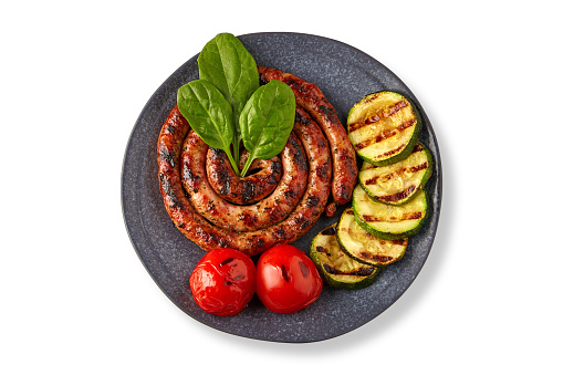 Fried spiral sausage with grilled vegetables and basil on a ceramic plate isolated on a white background. Top view with copy space.