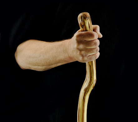 A man's hand holding the top of a walking stick or cane. Black background.