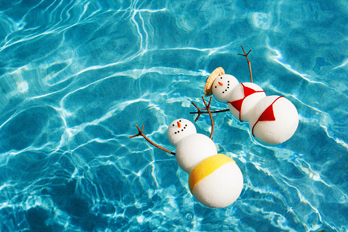 A couple of male and female snowman and snow woman in swimsuit vacationing in a tropical beach pool.