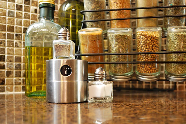 Spice Rack, Olive Oil, Salt and Pepper with Timer A rack of spices sits next to a half empty bottle of olive oil with a small salt and pepper shaker with a stainless steel timer in the foreground. Set against brown marble mosaic tiles and brown granite countertops. spice rack stock pictures, royalty-free photos & images