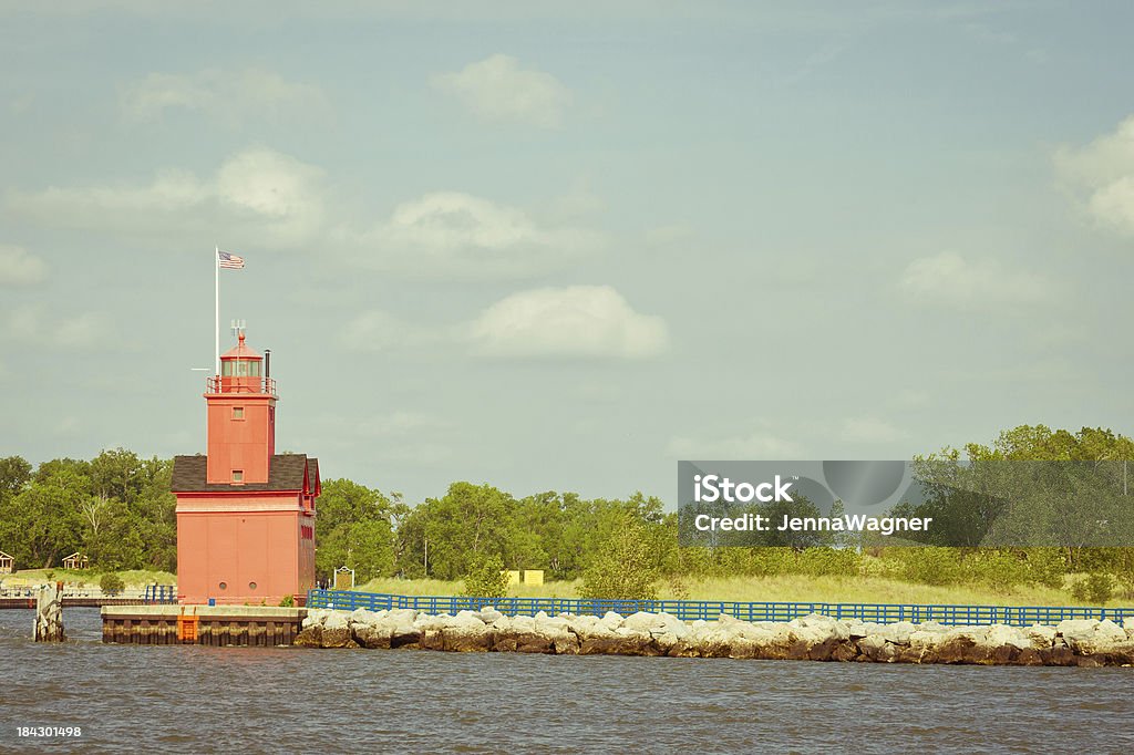 Big Red Lighhouse by Water "Big Red lighthouse with a blue handrail going down the jetty into the ocean. Summertime with blue sky and green trees. Sun is just starting to set, casting a bright glow over everything." Architectural Feature Stock Photo