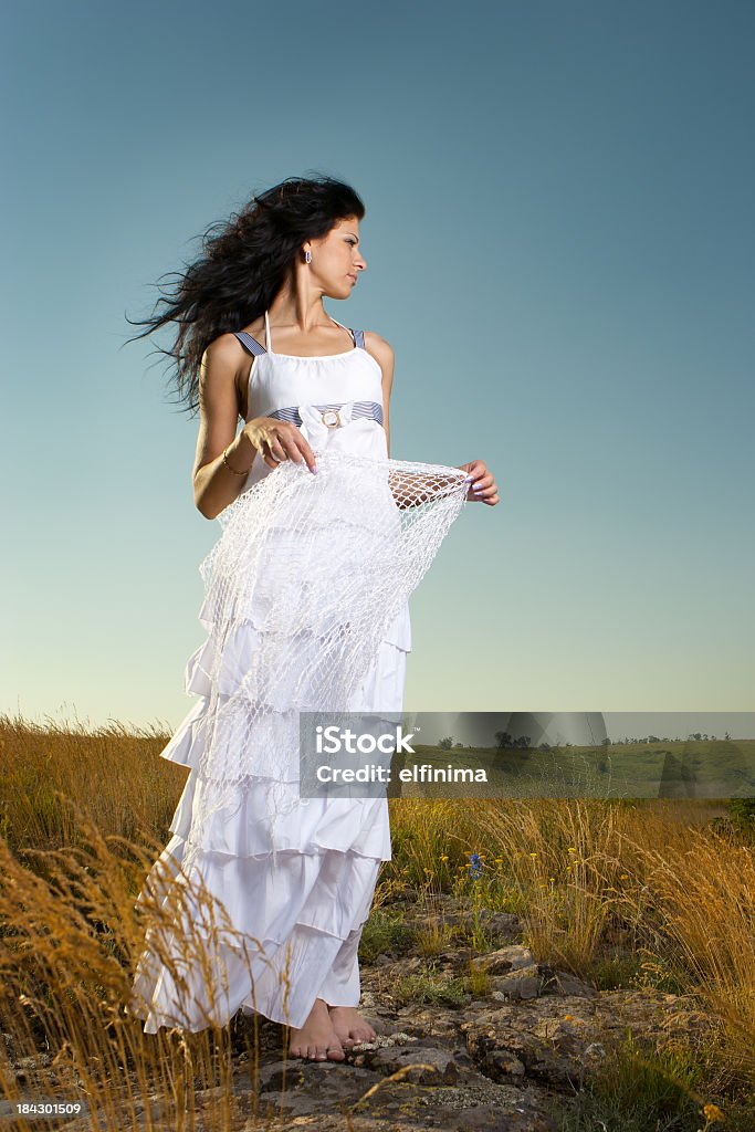 Hermosa mujer wearing white dress de pie en un campo - Foto de stock de Cielo libre de derechos