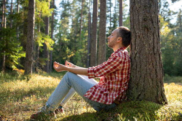 istock Man sitting under tree in forest with closed eyes meditating in unity with nature in sunny day. 1843020932
