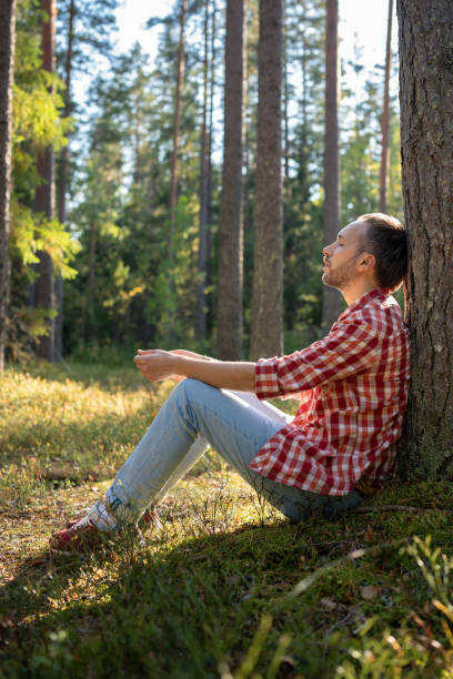 istock Carefree relaxing man sits on moss leaning against forest tree meditating during break from walk. 1843021220