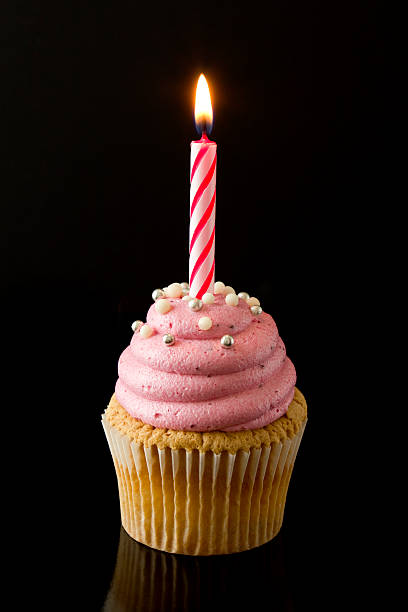 Party cupcake "Pink buttercream cupcake with single burning candle, on black background." cupcake candle stock pictures, royalty-free photos & images