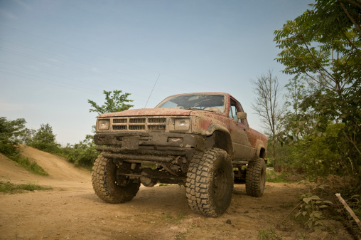 A 1984 Toyota pickup truck covered with mud on dirt trails.