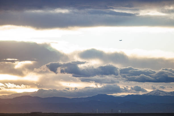 An airplane disappears into the distance as the golden light of the setting sun casts an orange glow on the dark clouds.