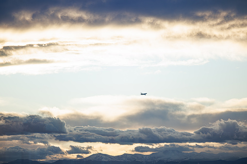 An airplane disappears into the distance as the golden light of the setting sun casts an orange glow on the dark clouds.