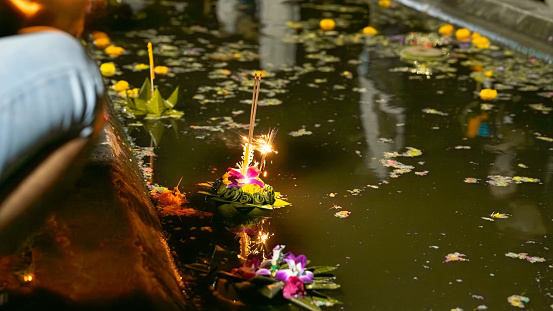 Photograph of 3 banana-leaf and orchid-flowering krathongs floating in a water source that is not very clean. Because it was full of flower scraps and banana leaves, at night there was a dim light