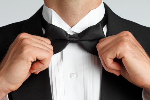 A close up of a man in a tuxedo adjusting his bow tie.