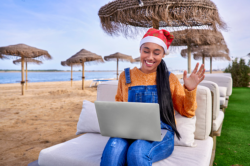 Colombian Latin YouTuber girl with her laptop greets her subscribers on Christmas Day from the beach