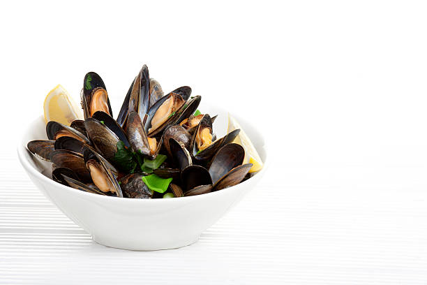 A bowl of mussels garnished with lemons on a white table  stock photo