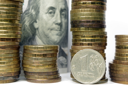 One ruble coin and stacks of different heights against the background of Franklin's dollar portrait