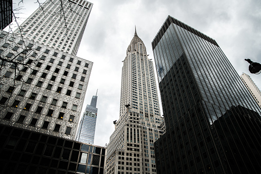 Low angle of high multistory buildings and Chrysler building located in central district of New York City against cloudy gloomy sky