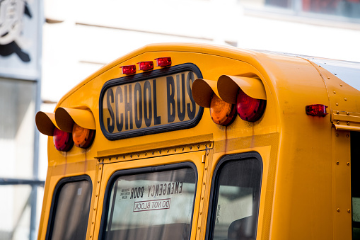 Yellow school bus with headlights parked near building on street on sunny day in New York