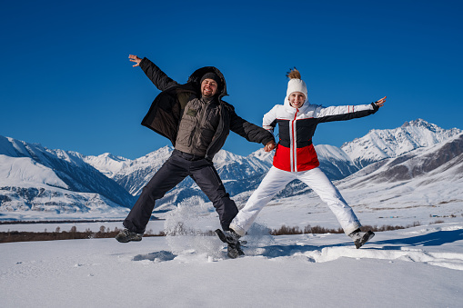 Young happy man and woman jumping on mountains background in winter season