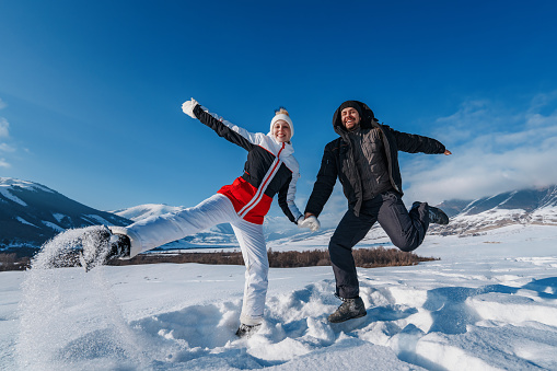 Young happy man and woman jumping on mountains background in winter season