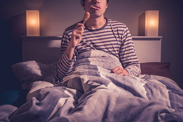 Young man is sitting in bed and eating chicken stock photo