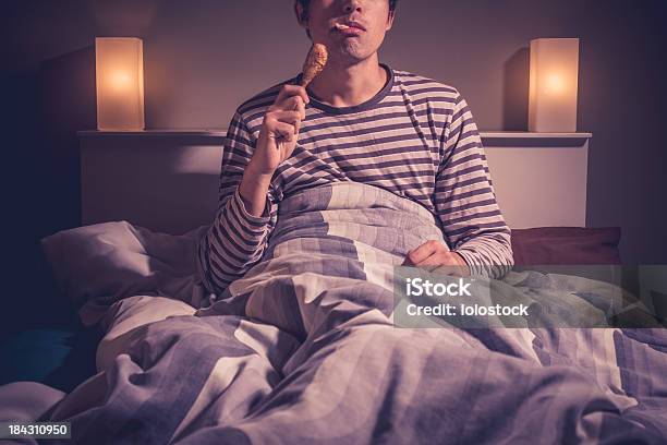 Young Man Is Sitting In Bed And Eating Chicken Stock Photo - Download Image Now - Bed - Furniture, Eating, Night