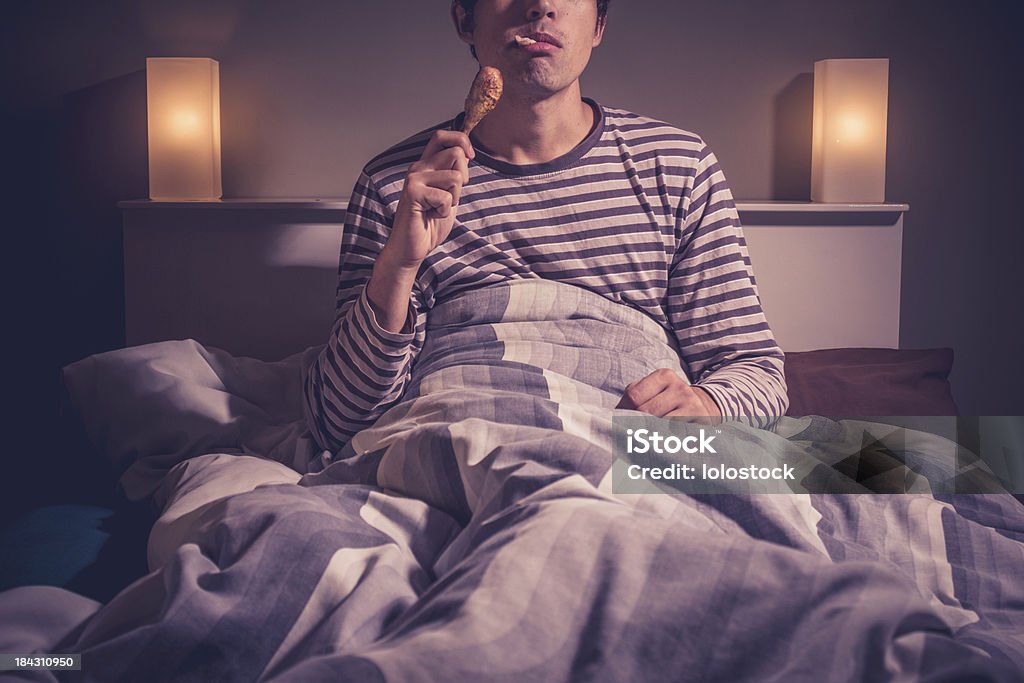 Jovem sentada na cama e comer de frango - Foto de stock de Cama royalty-free