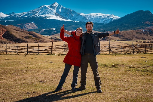Tourist couple posing with thumbs up on high mountains background