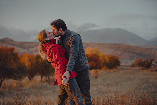 Happy young couple kissing on mountains background in autumn