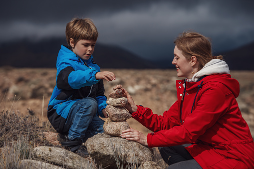 Young woman with her son build a pyramid of stones in the mountains