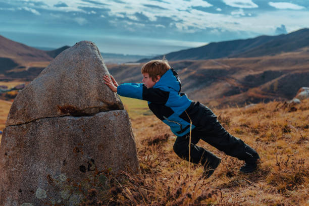 Boy is trying to move a big stone in the mountains