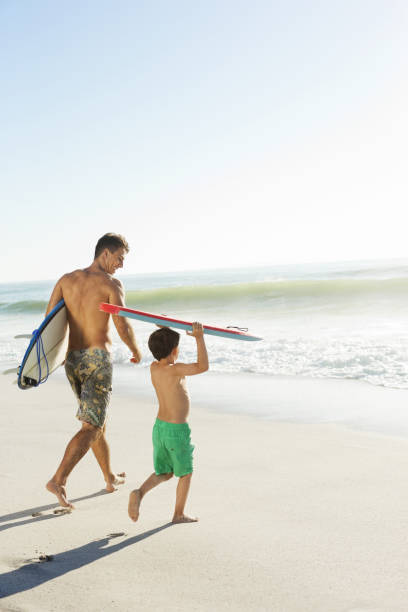 istock Father and son carrying surfboard and bodyboard on beach 184313311