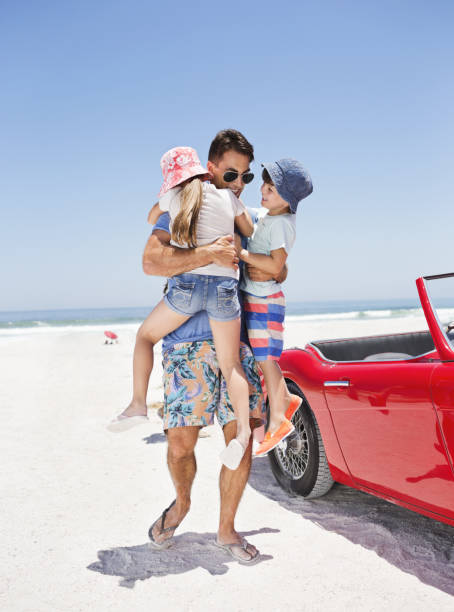 istock Father hugging children on beach next to convertible 184313340