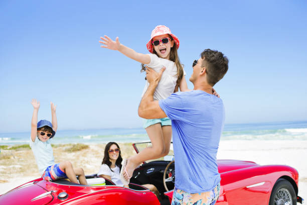 istock Father lifting daughter from convertible at beach 184313394