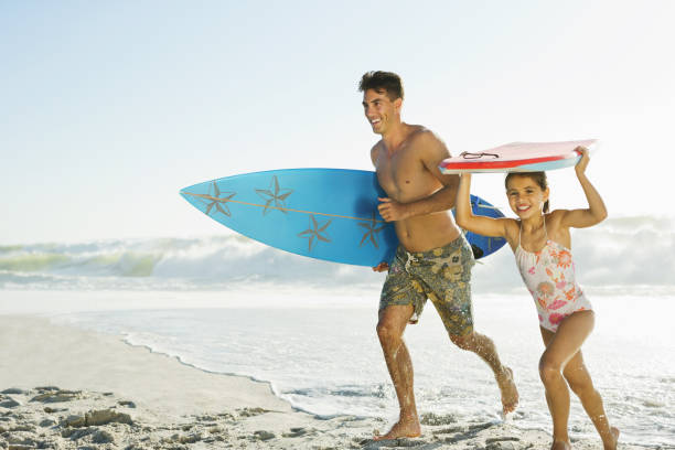 istock Father and daughter carrying surfboard and bodyboard on beach 184313400
