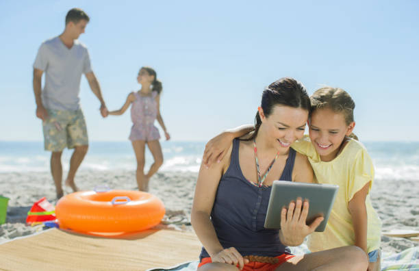 mère et fille à l'aide de tablette numérique sur la plage - reading beach e reader men photos et images de collection