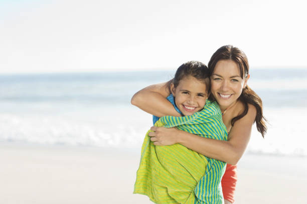istock Mother wrapping daughter in towel on beach 184313473