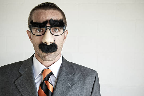 Businessman wearing disguise specs with thick eyebrows and mustache looks at camera with blank expression