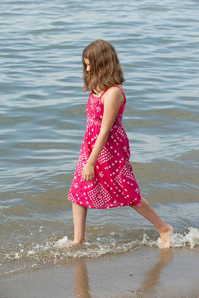 joven adolescente entretela a lo largo de la orilla del lago. - wading child beach sundress fotografías e imágenes de stock