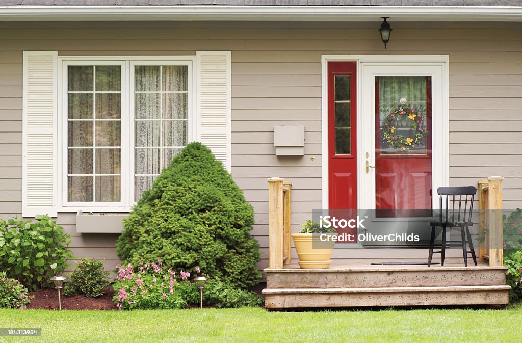 Porch seat. A small deck and steps in front of a residential house in Prince Edward Island, Canada. Pictured during the early Summer. An inviting black chair is sits beside the front door. Architectural Feature Stock Photo