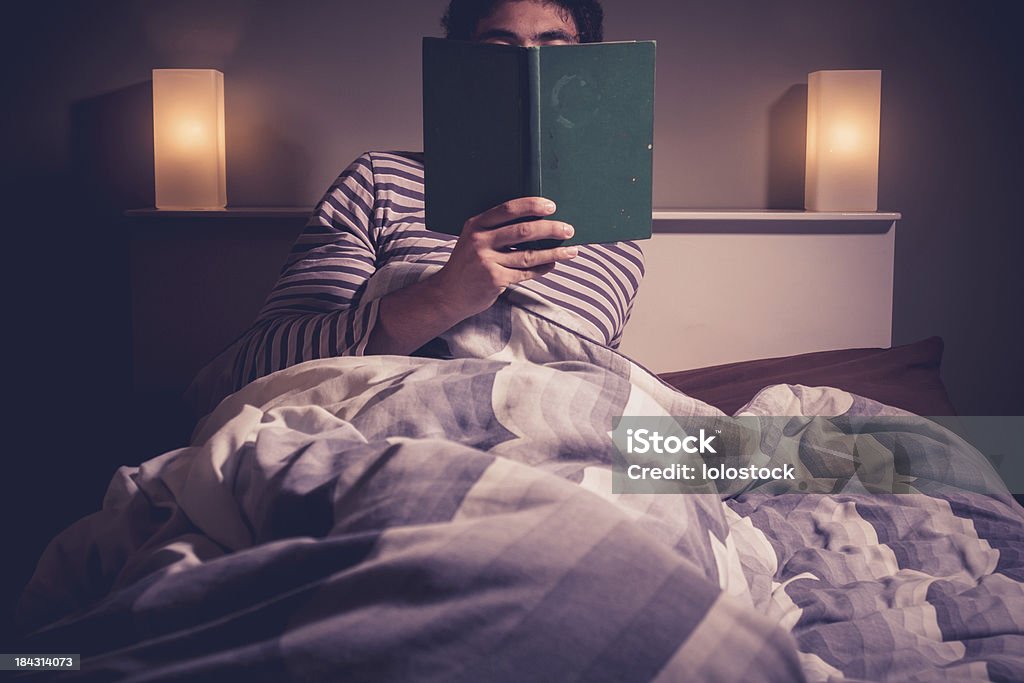 Молодой человек, чтение в постели - Стоковые фото Кров�ать роялти-фри