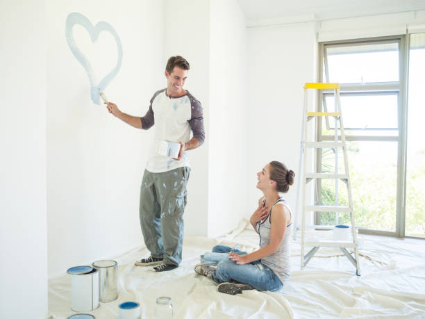 istock Woman watching man paint blue heart on wall 184314602
