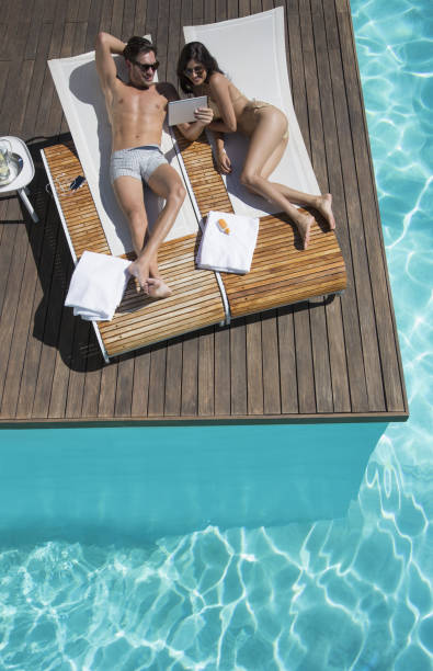 pareja relajándose en sillas reclinables en la piscina - swimming trunks bikini swimwear red fotografías e imágenes de stock
