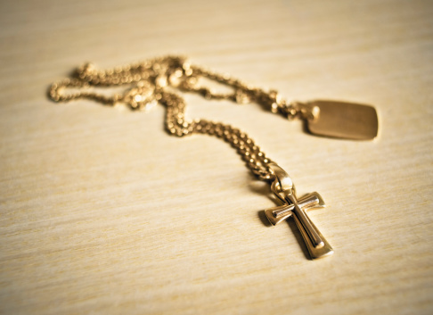 Gold crucifix necklace on a wooden table. The image is processed from 16 bit RAW files in sRGB colorspace, as possible to maintain the color fidelity.