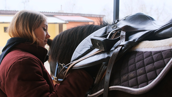 The young woman adjusted the saddle on the brown horse.