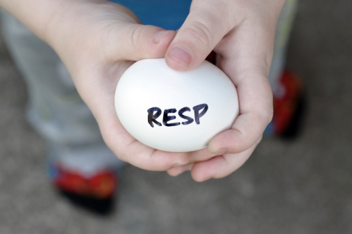 Close up of a 2 year old boy holding an egg that reads RESP. An RESP is a Registered Education Savings Plan and the egg symbolizes saving for a child's education in Canada. See also