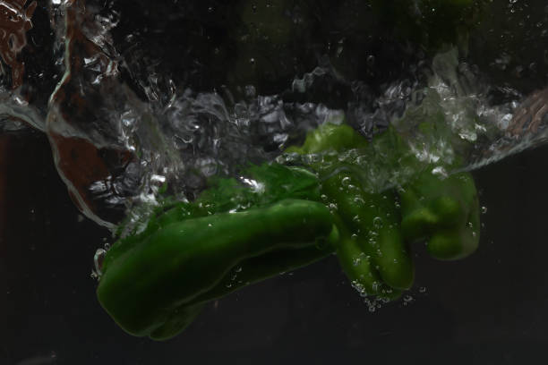 green peppers falling into water with splashes of water on black background.