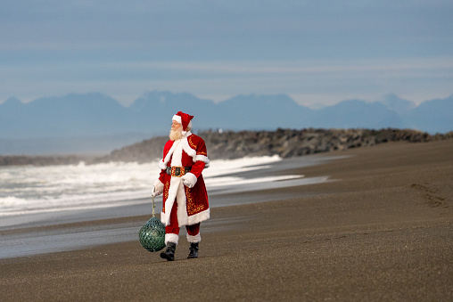 Santa Claus with glass buoy on beach with surf