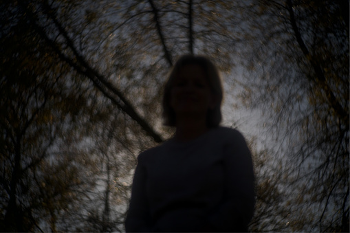This photograph depicts a blurred silhouette of a woman standing against a backdrop of trees, creating a soft and mysterious atmosphere.