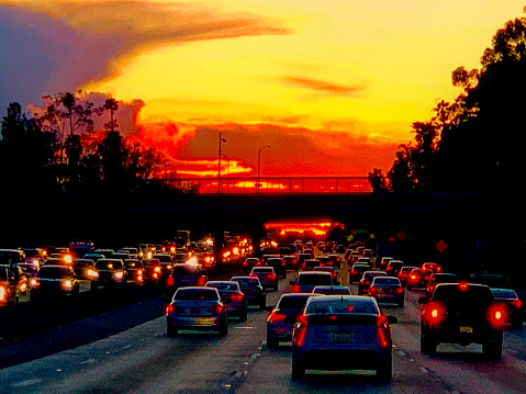 This photograph captures a busy freeway  at sunset after a big storm, with cars and trucks driving home at rush hour.