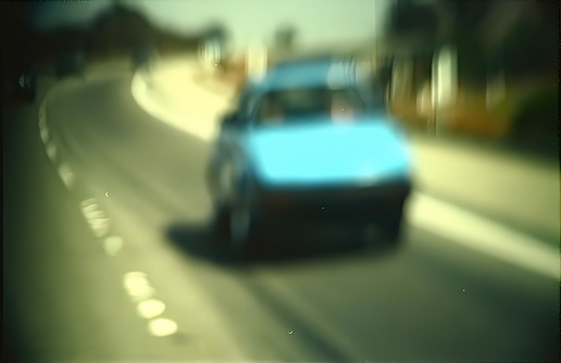 This photograph depicts a blurred image of a car, captured in a rearview mirror, with a backdrop of indistinct street scenery.